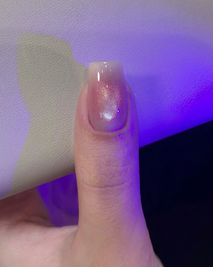Ein Daumen unter violettem UV/LED-Lampenlicht, der das frisch magnetisierte Cat-Eye-Nageldesign aushärtet.