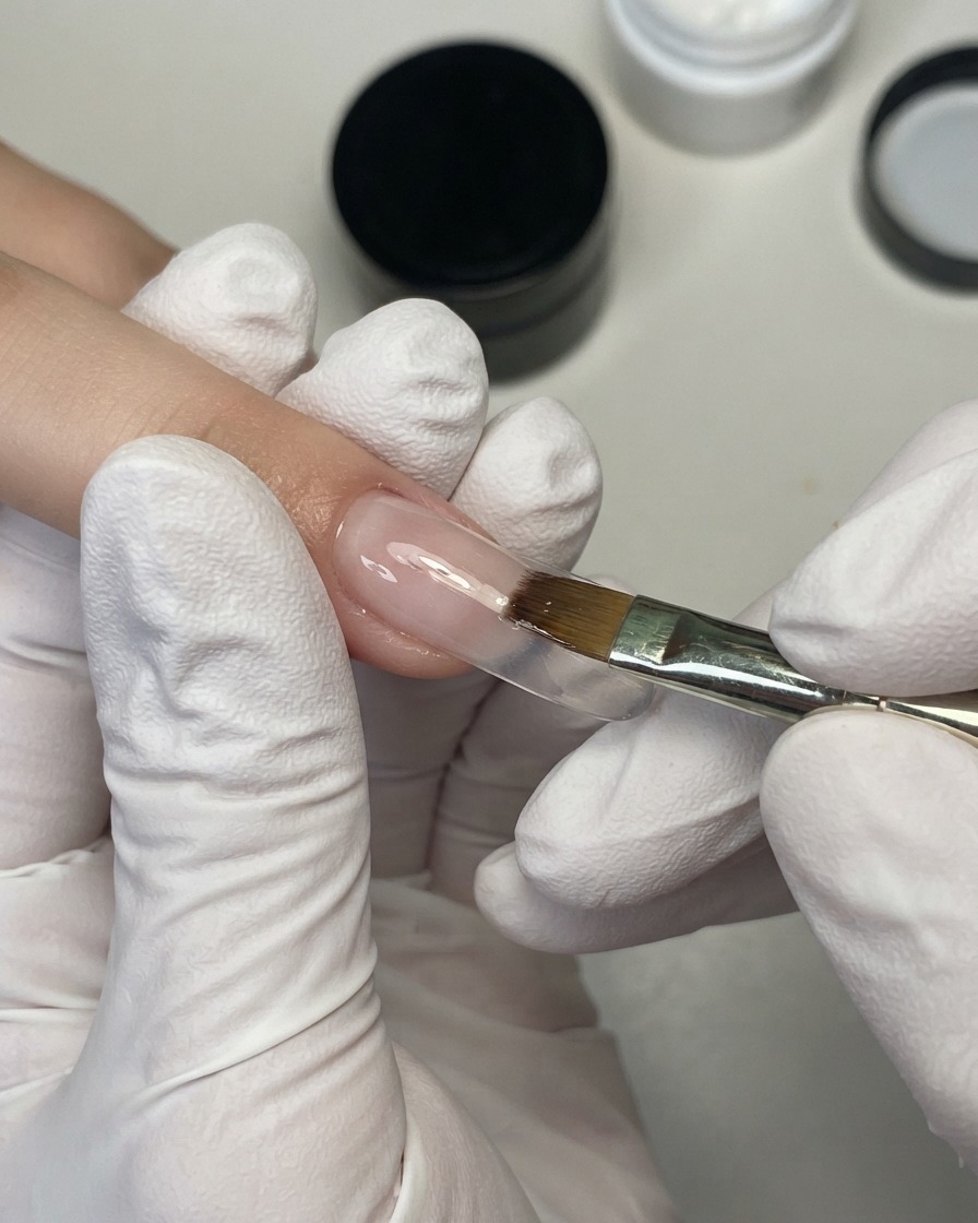 Ein weicher Nagelpinsel verblendet einen peachy-nude Gel-Farbverlauf nach oben auf der Nageloberfläche.