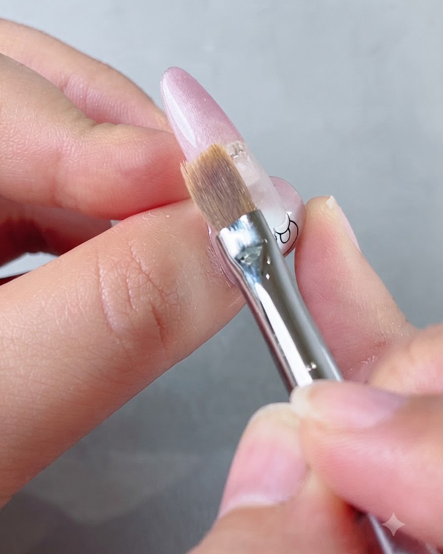 Nahaufnahme eines weichen Flachpinsels, der rosa Gel-Lack sanft nach unten auf einem Fingernagel verblendet.