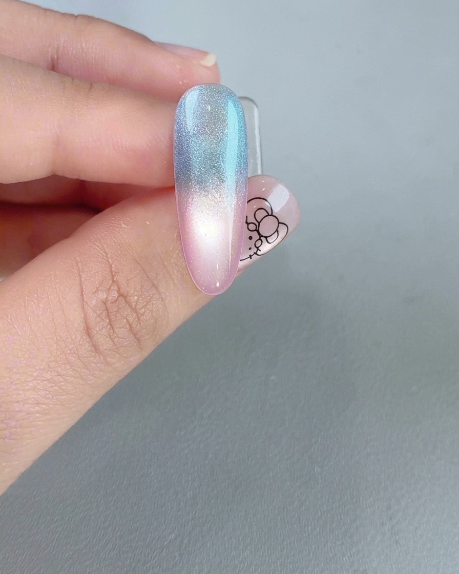 Ein fertiger Nagel zeigt eine helle, leuchtende Cat-Eye-Reflektion über einem Rosa-Blau-Farbverlauf.