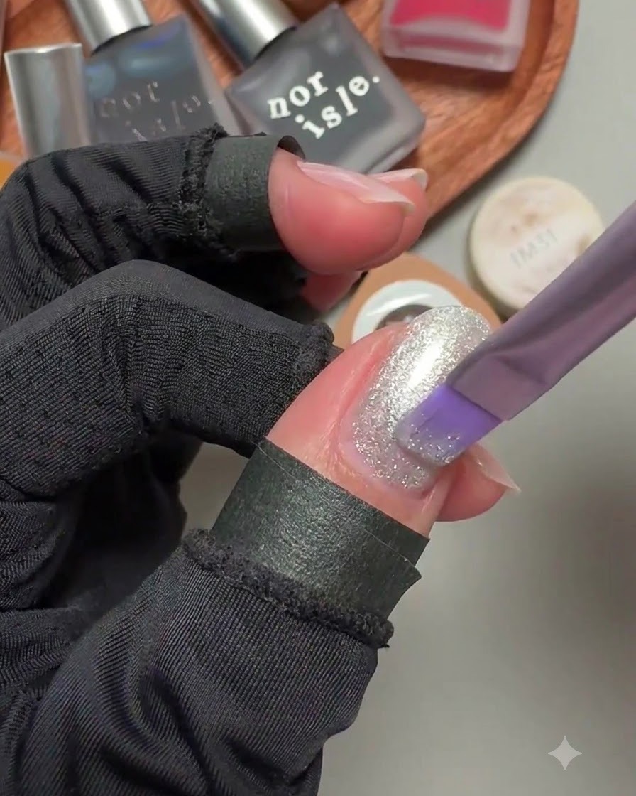 Ein Pinsel trägt einen schimmernden silbernen Cat-Eye-Gel-Lack auf einen Fingernagel auf.
