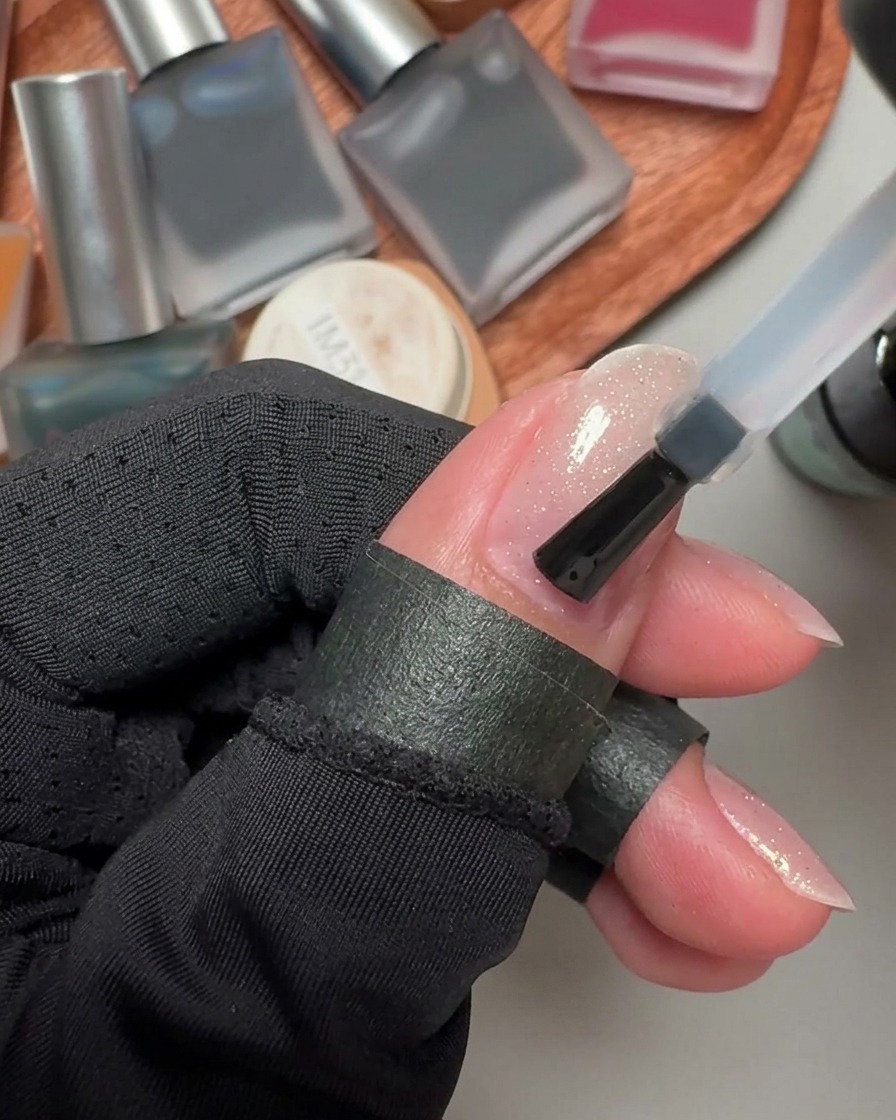 Ein Nagellackpinsel trägt eine klare, feuchte Schicht Base-Coat-Gel auf einen Fingernagel auf.