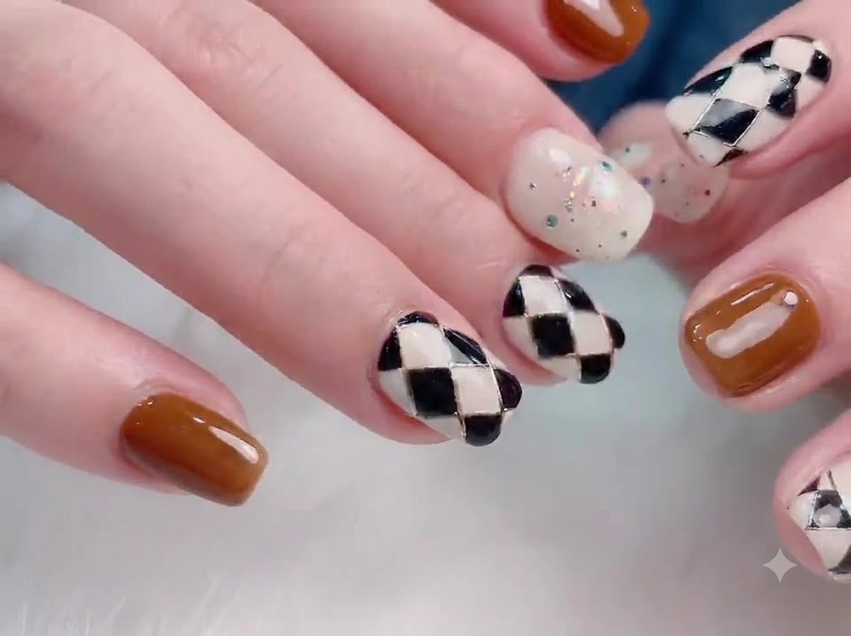 Eine Nahaufnahme einer Hand mit glatten, einfarbigen braunen Nägeln gepaart mit einem cremefarbenen Polka-Dot-Akzentnagel.
