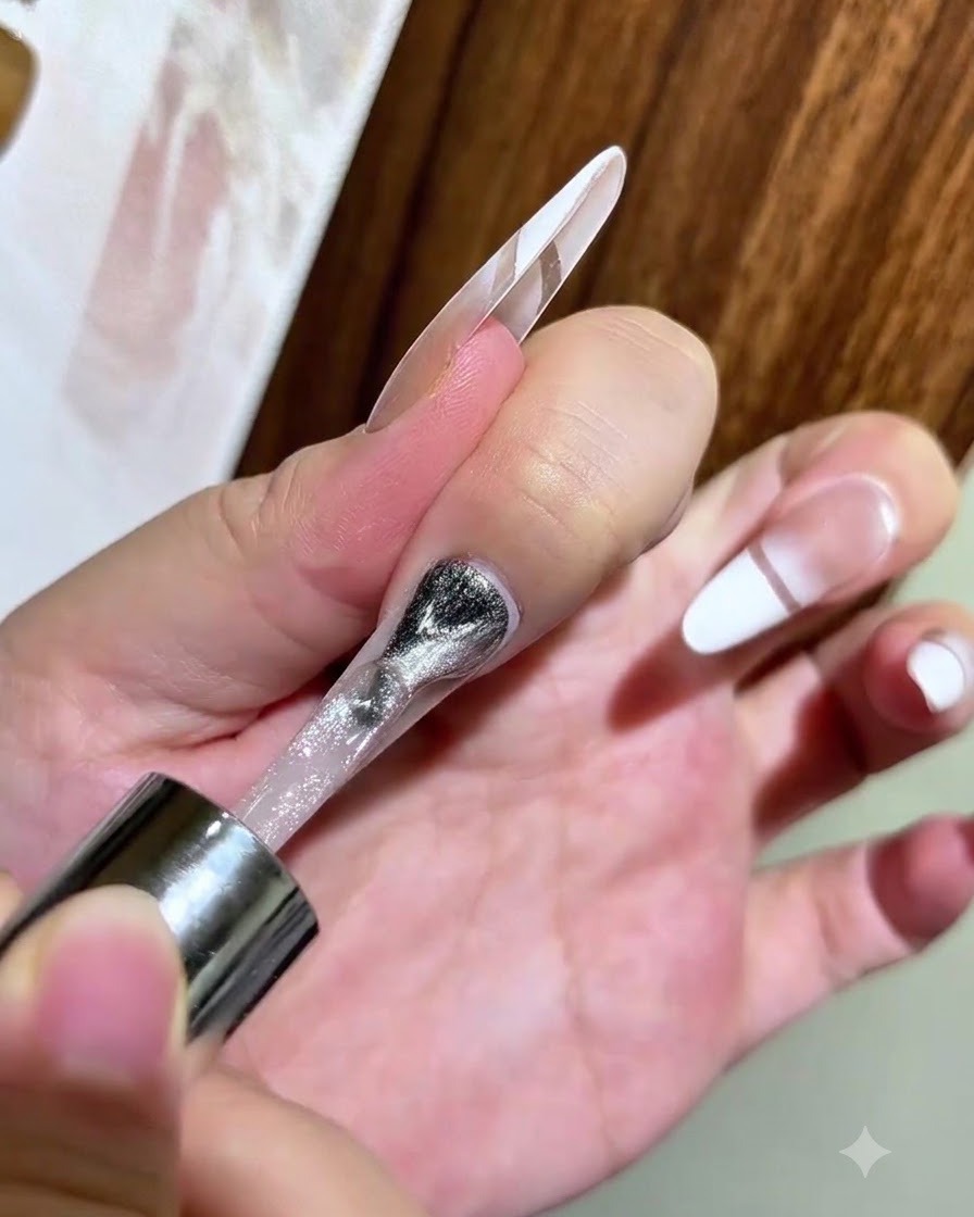 Ein Nagellackpinsel trägt silbernes Magnet-Cat-Eye-Gel auf einen klaren Nagel mit verblendeter weißer Spitze auf.