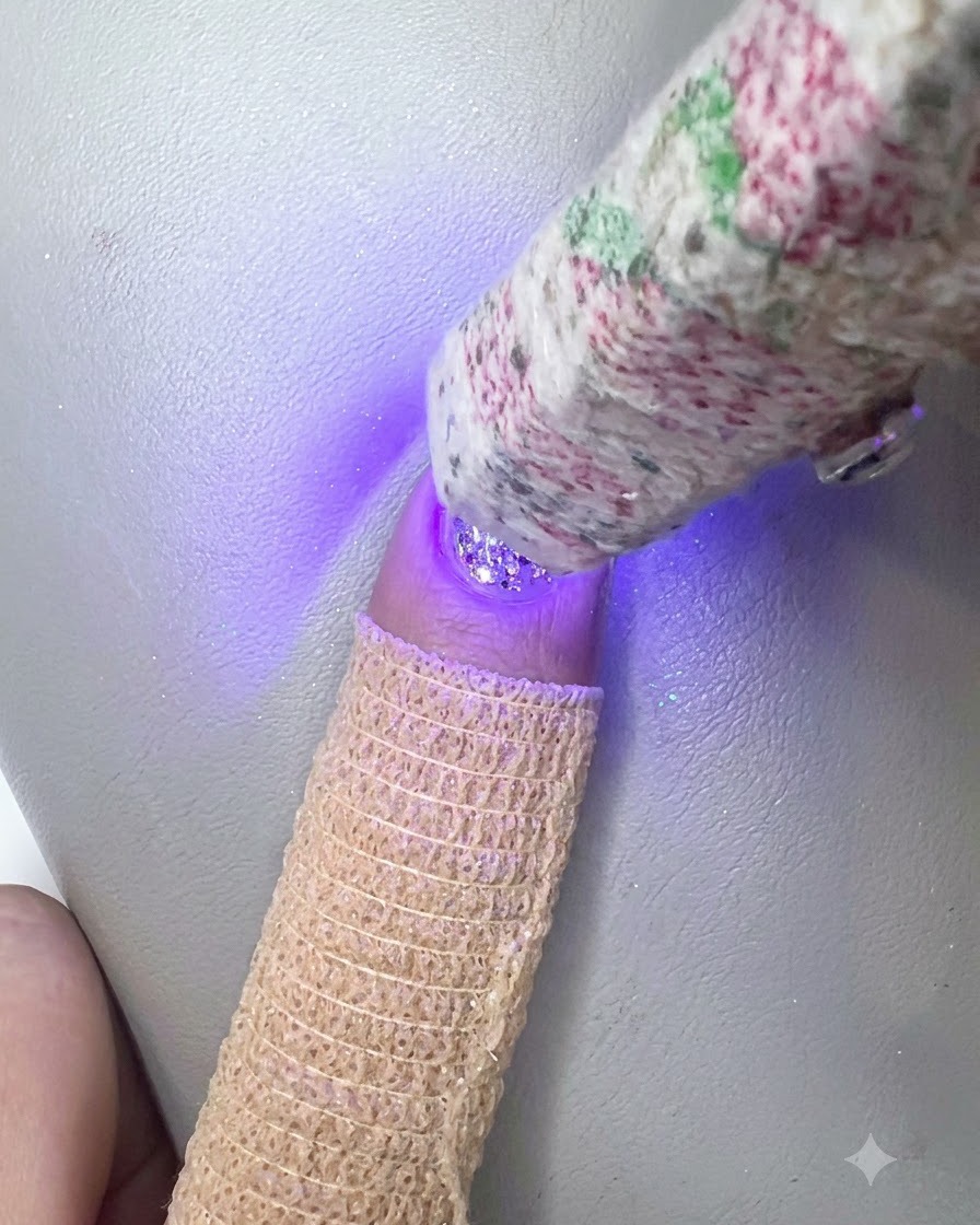 Eine handgehaltene UV-LED-Lampe härtet die klare Builder-Gel-Schicht über dem Glitternagel aus.