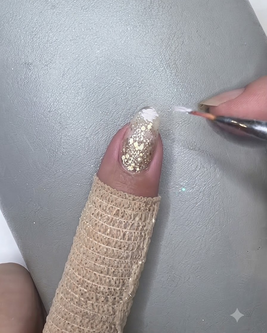 Ein Pinsel tupft elfenbeinweißes Gel sanft auf die Nagelspitze, um einen Farbverlauf zu erzeugen.